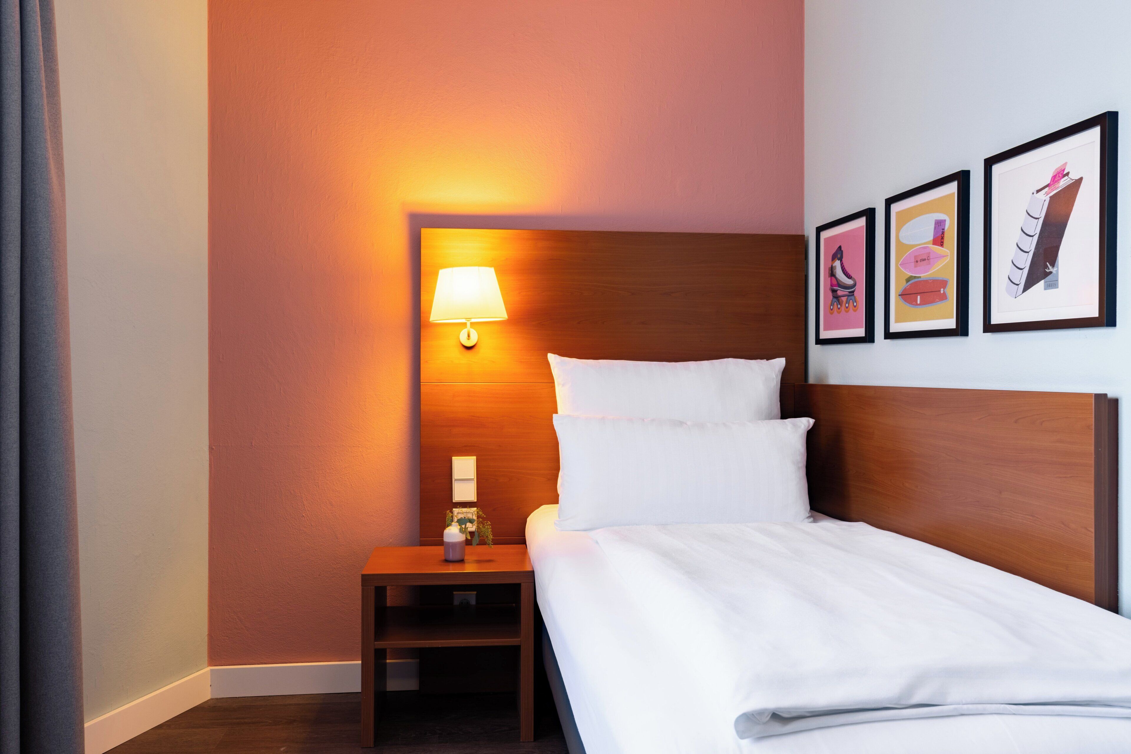 Une chambre d’hôtel avec une tête de lit en bois, une lampe de chevet, une table de chevet et trois tableaux encadrés accrochés au mur.