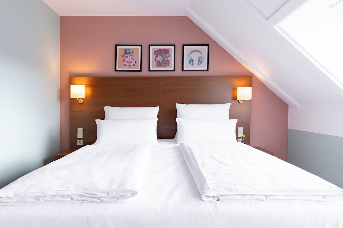 A double bed with white linens, two bedside lamps, and three framed pictures on the wall.
