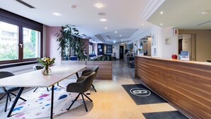 Een hotel receptie met een houten balie, een zithoek met stoelen en een tafel, en een groot raam dat uitzicht biedt op het omliggende landschap.