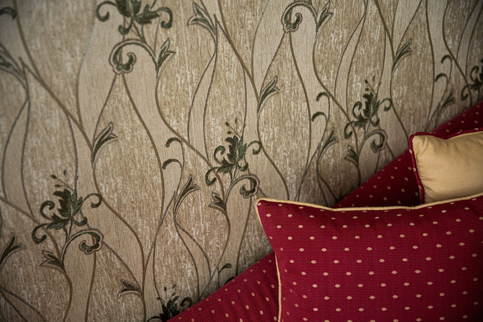 A close-up of a textured wall with a floral pattern and a red polka-dotted pillow.