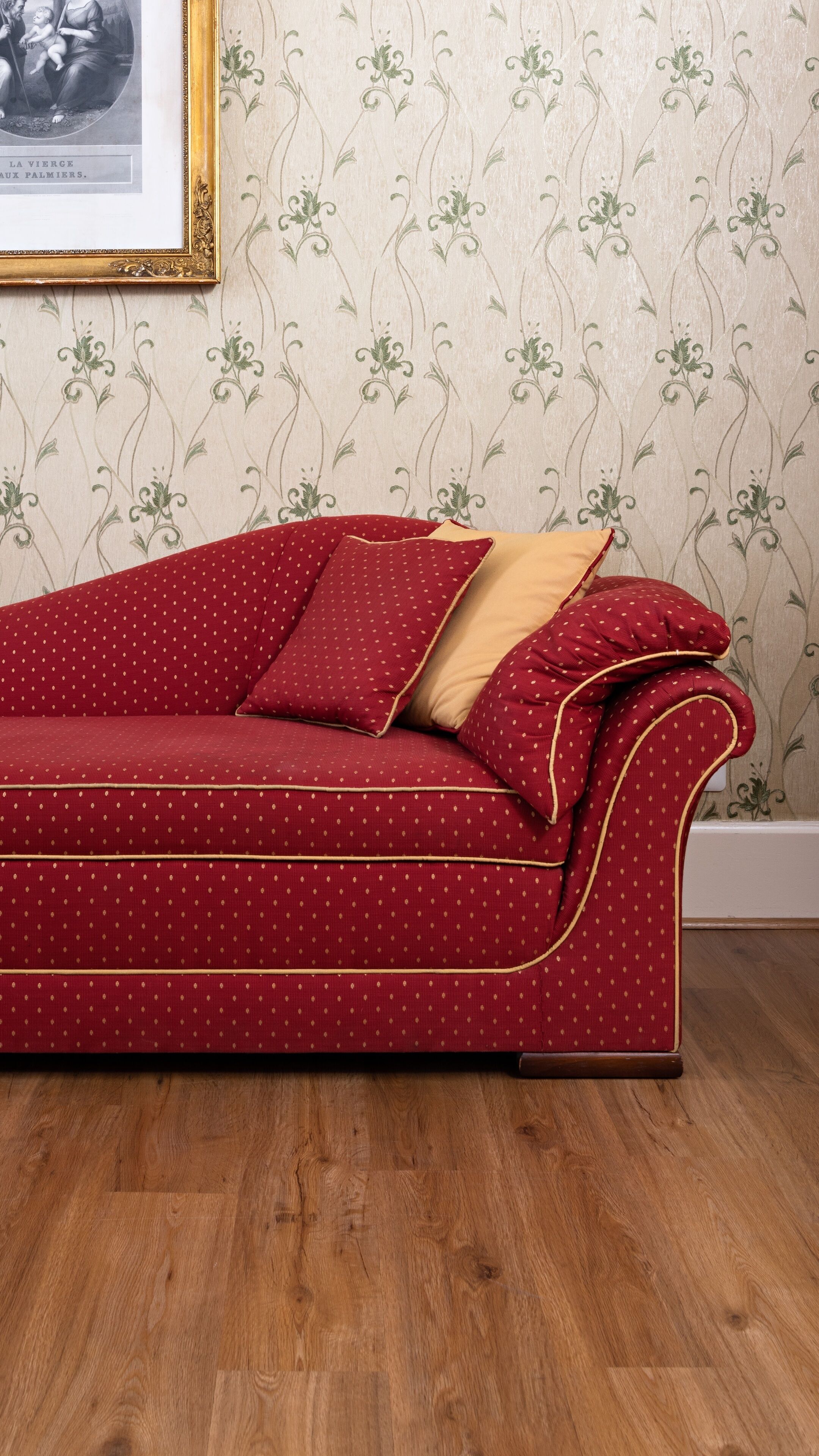 Ein rotes Sofa mit Goldverzierungen und Punkten, vor einem Blumenmuster-Tapeziertem Wand.