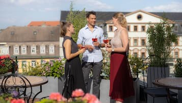 Una terraza en la azotea con mobiliario exterior, vistas a edificios y cielo despejado.