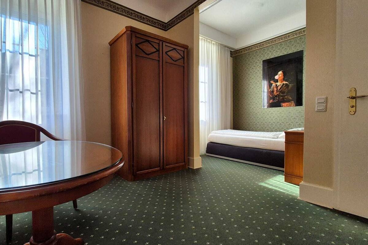 Una habitación de hotel con una mesa redonda de vidrio, un armario de madera, una cama y un cuadro en la pared.