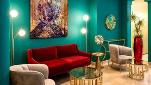 Een kamer in teal met een rode bank, twee fauteuils, een glazen salontafel en een schilderij aan de muur.