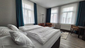 Een hotelkamer met twee bedden, een bureau, een stoel en grote ramen voorzien van gordijnen.