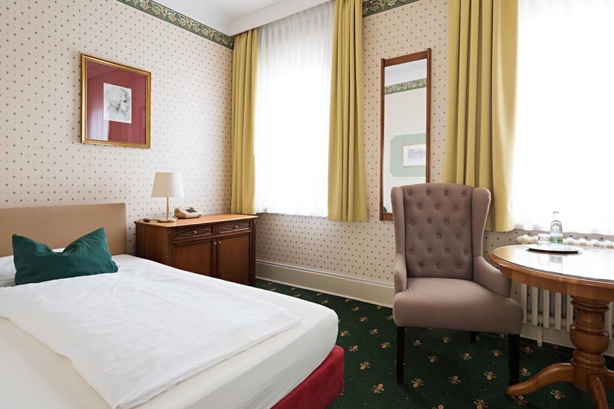 Habitación de hotel con cama, una silla, una mesa, cómoda y espejo.