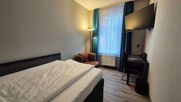 Ein Hotelzimmer mit Bett, Schreibtisch, Stuhl, Fernseher und einem Fenster mit Vorhängen.