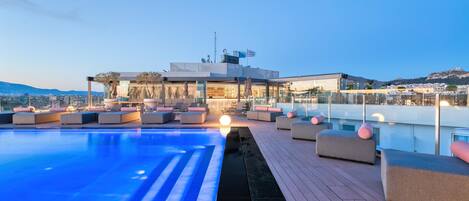A rooftop pool area with lounge seating and a view of the cityscape.