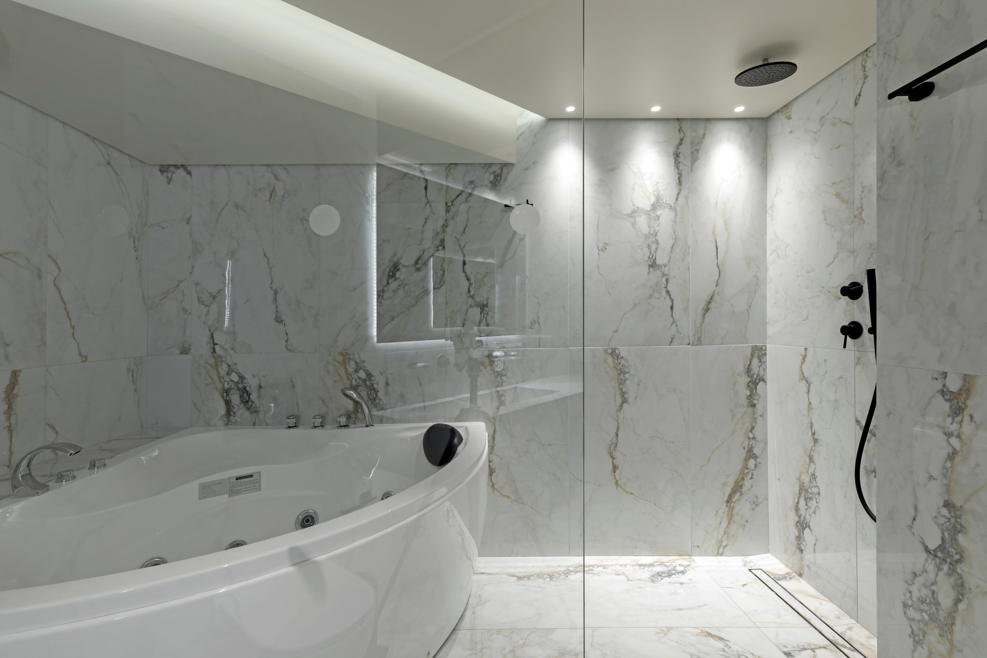 A modern bathroom with a freestanding bathtub, a glass-enclosed shower area, and marble walls.