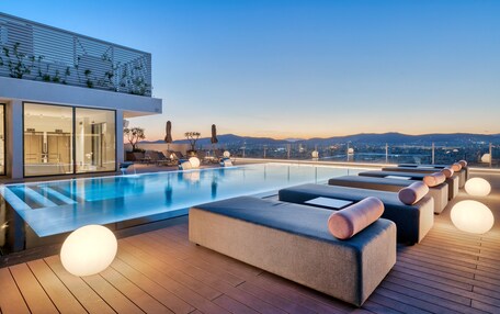 A rooftop pool area with modern loungers and a city view.