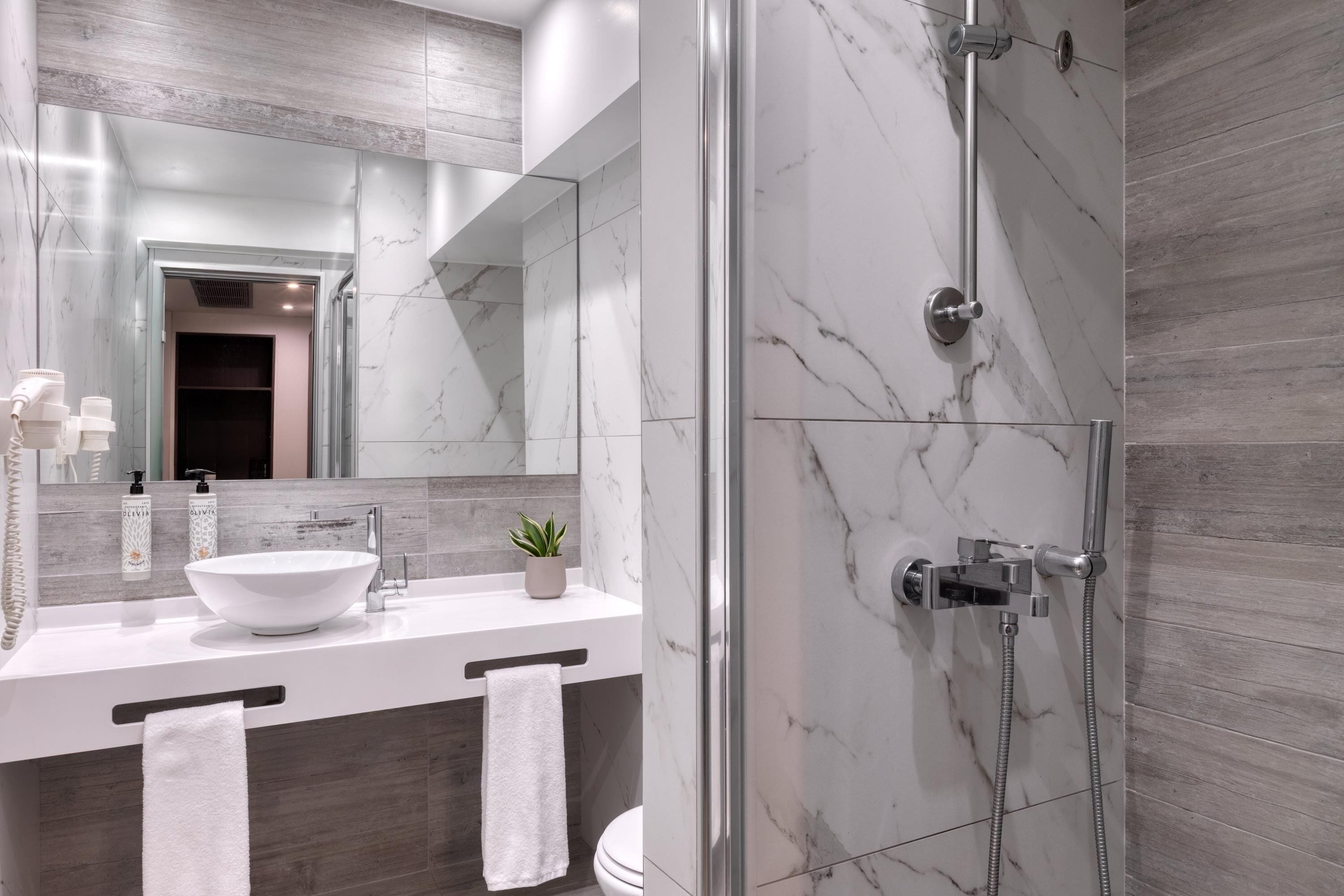 Un baño moderno con un lavamanos blanco, un espejo grande y una ducha con cerramiento de vidrio.