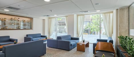 A modern lobby with seating areas, a display of pottery, and large windows with curtains.