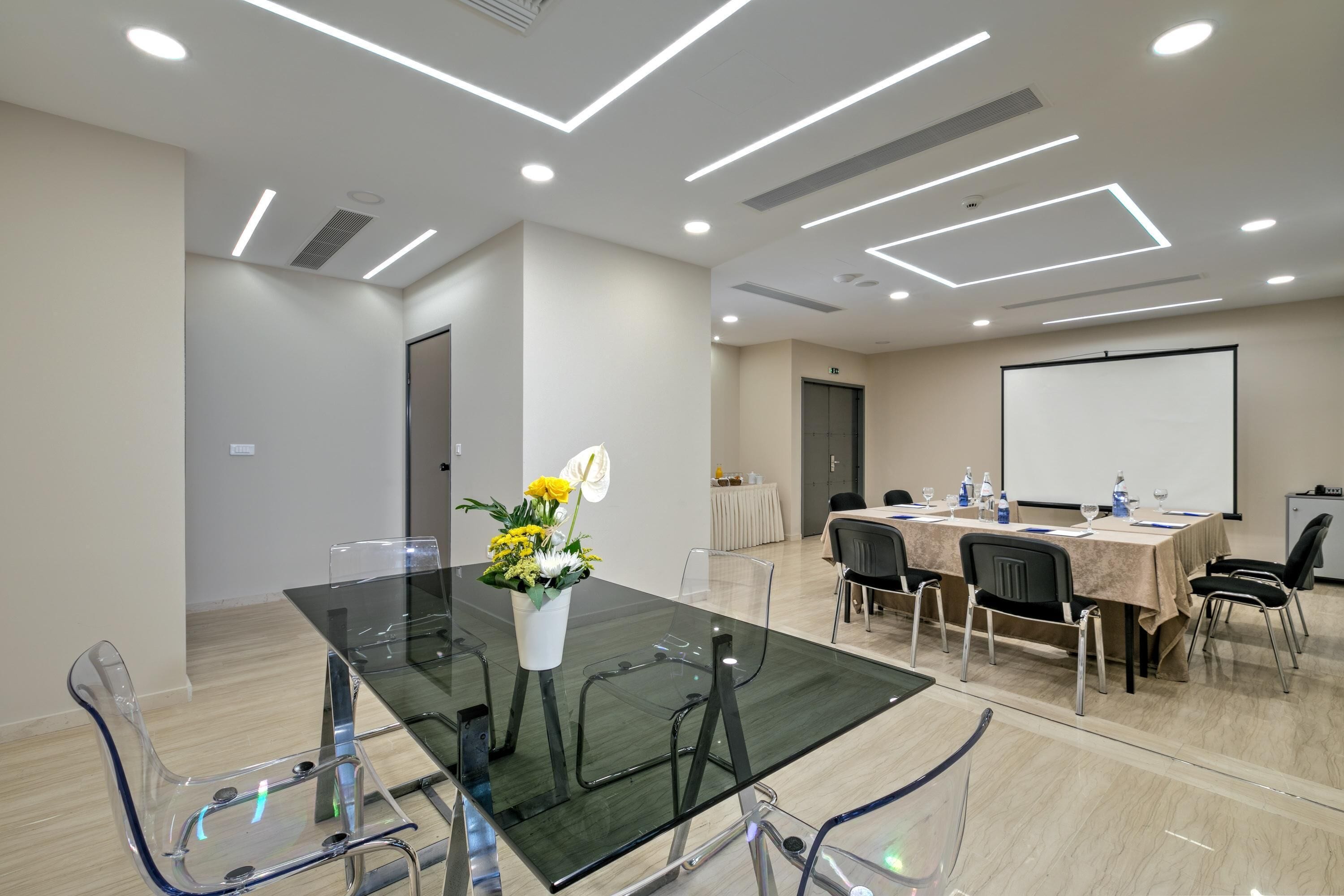 Une salle de conférence équipée d’une table en verre, de chaises transparentes, d’un tableau blanc et d’un écran de projection.