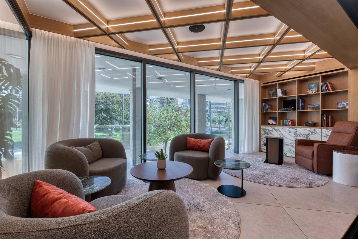 A modern living room with a large glass door leading to a balcony, furnished with sofas and a coffee table, and a marble bookshelf.