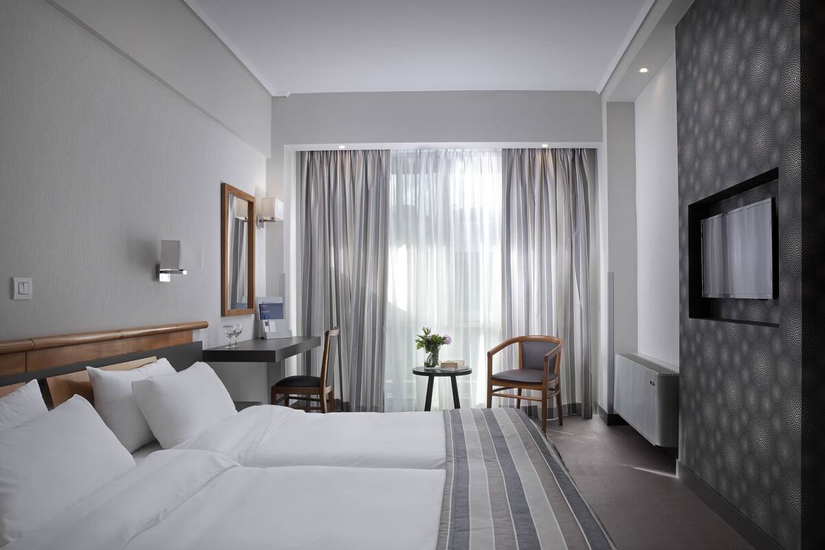 A hotel room with a bed, a desk, a chair, a TV, and a window with curtains.