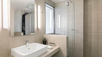 Une salle de bain moderne avec un grand lavabo blanc, une cabine de douche en verre et une petite plante en pot posée sur le meuble-lavabo.
