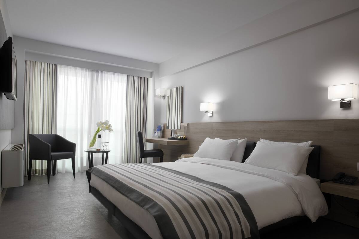 A hotel room with a large bed, a desk, a chair, and a TV.