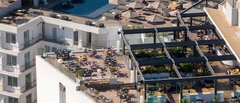A rooftop pool area with multiple sun loungers and umbrellas, surrounded by outdoor seating and dining areas.