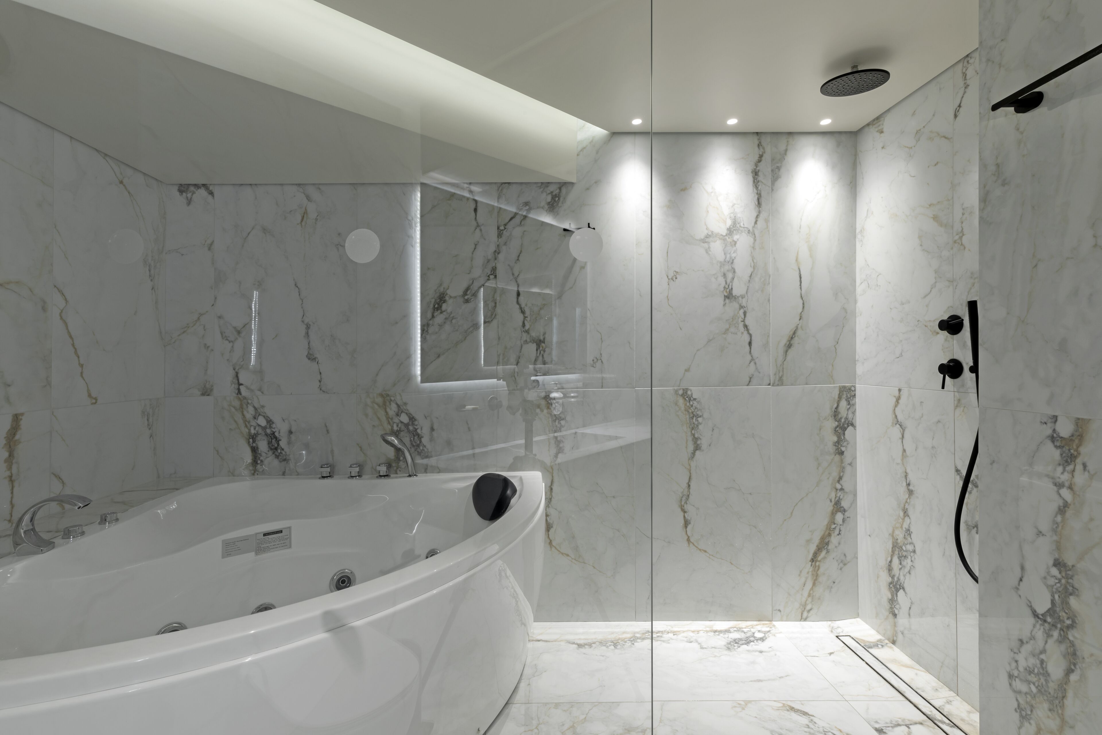 A modern bathroom with a freestanding bathtub, a glass-enclosed shower, and marble walls.