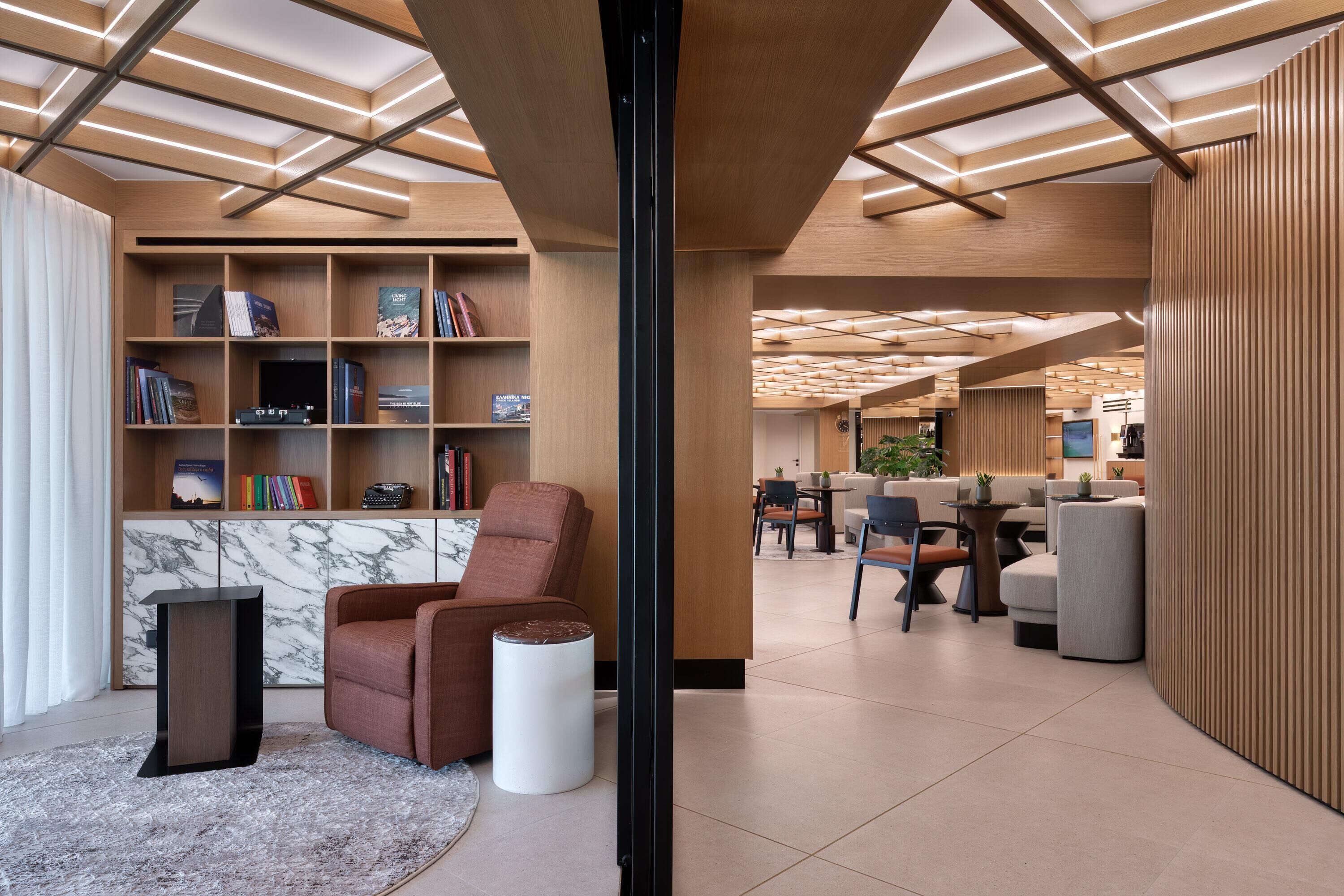 Un intérieur moderne avec une bibliothèque en bois, un mur d’accent en marbre, un fauteuil en cuir marron et une petite table d’appoint blanche.