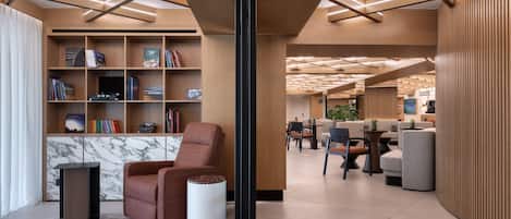 Un intérieur moderne avec une bibliothèque en bois, un mur d’accent en marbre, un fauteuil en cuir marron et une petite table d’appoint blanche.