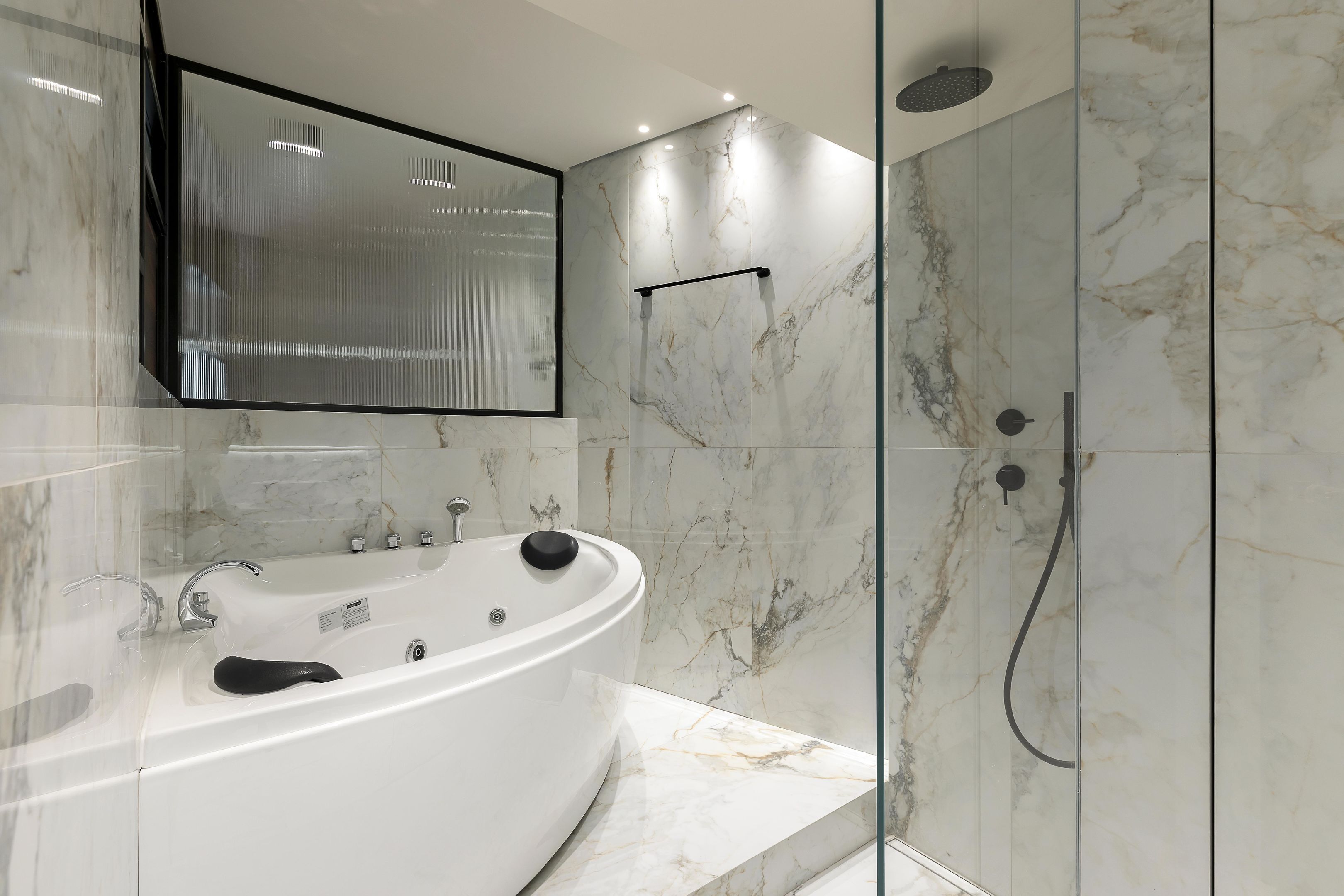 A modern bathroom with a freestanding bathtub, a glass-enclosed shower, and marble walls.