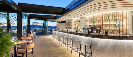 A bar area with a marble counter, bar stools, and a view of the cityscape.
