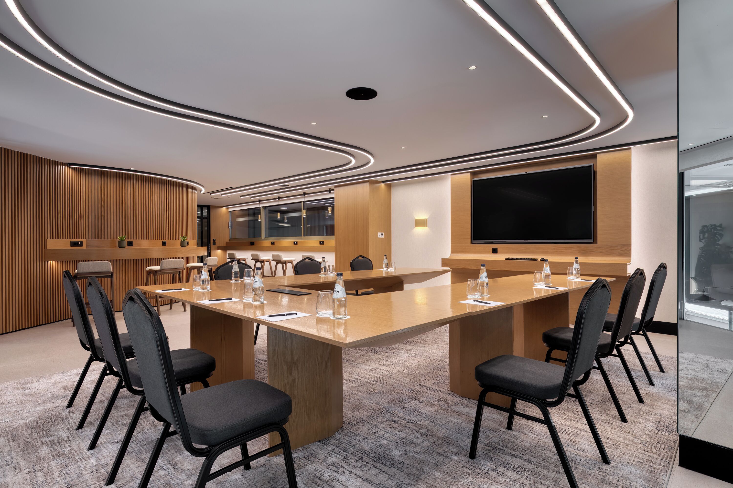 A modern conference room with a large table, chairs, and a flat-screen TV.