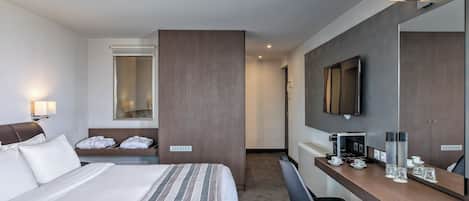 A hotel room with a bed, a desk with a coffee maker, a chair, a TV, and a mirror.