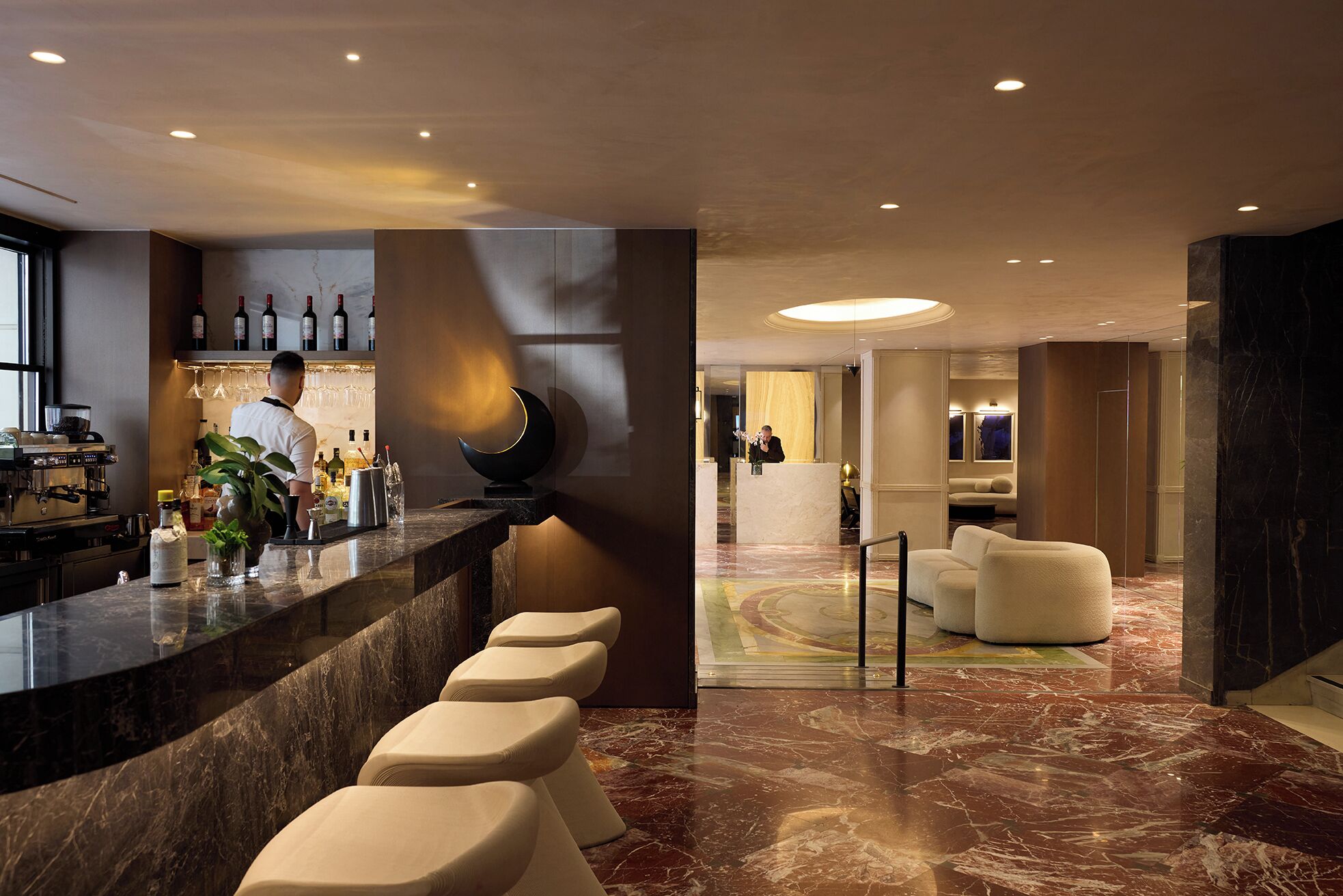 A modern hotel lobby with a marble reception desk, bar area, and seating.
