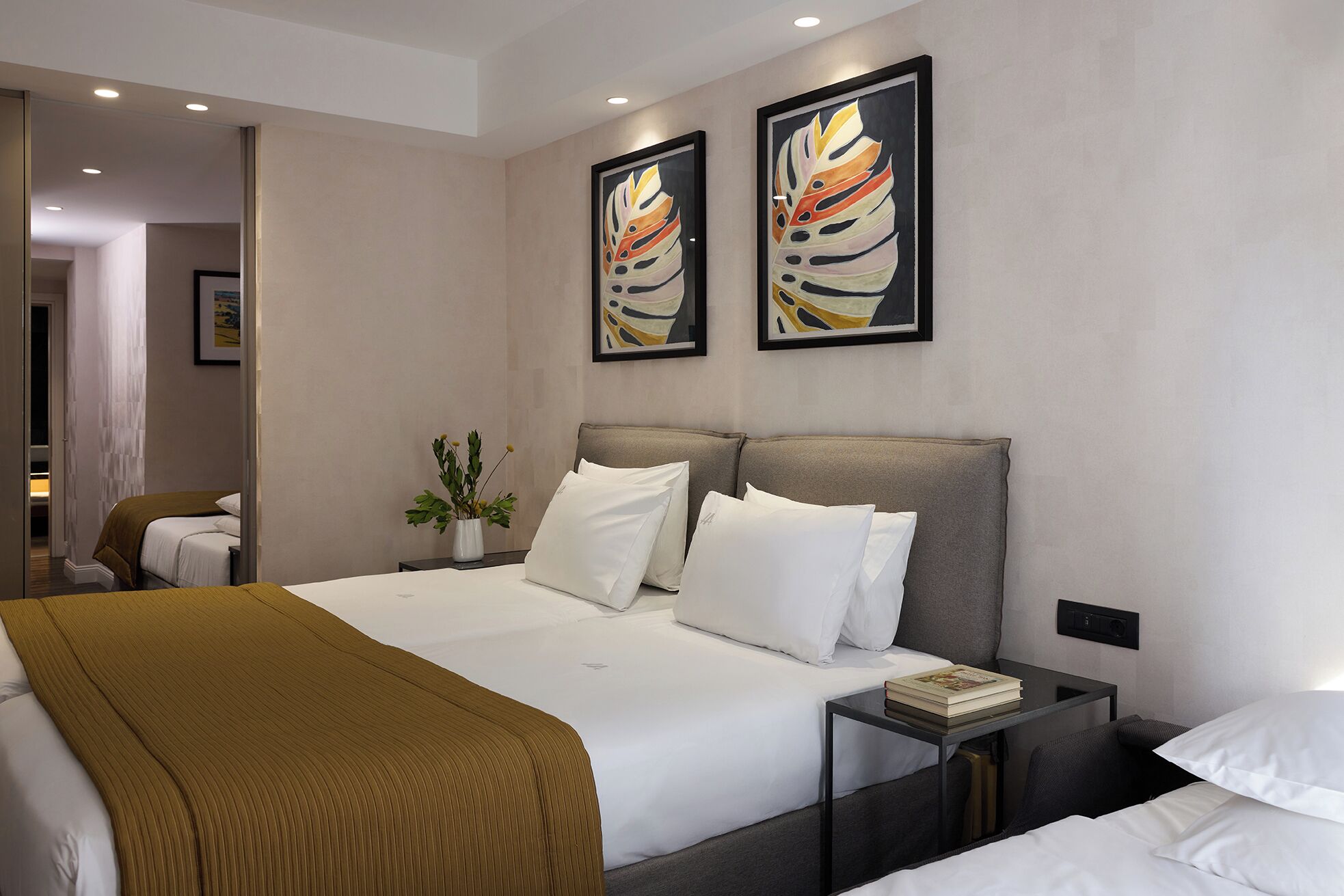A hotel room with a large bed, a bedside table with a book, and two abstract paintings on the wall.