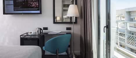 Ein Hotelzimmer mit Bett, Schreibtisch, Stuhl, Fernseher, Spiegel, Lampe und einem Balkon mit Geländer.