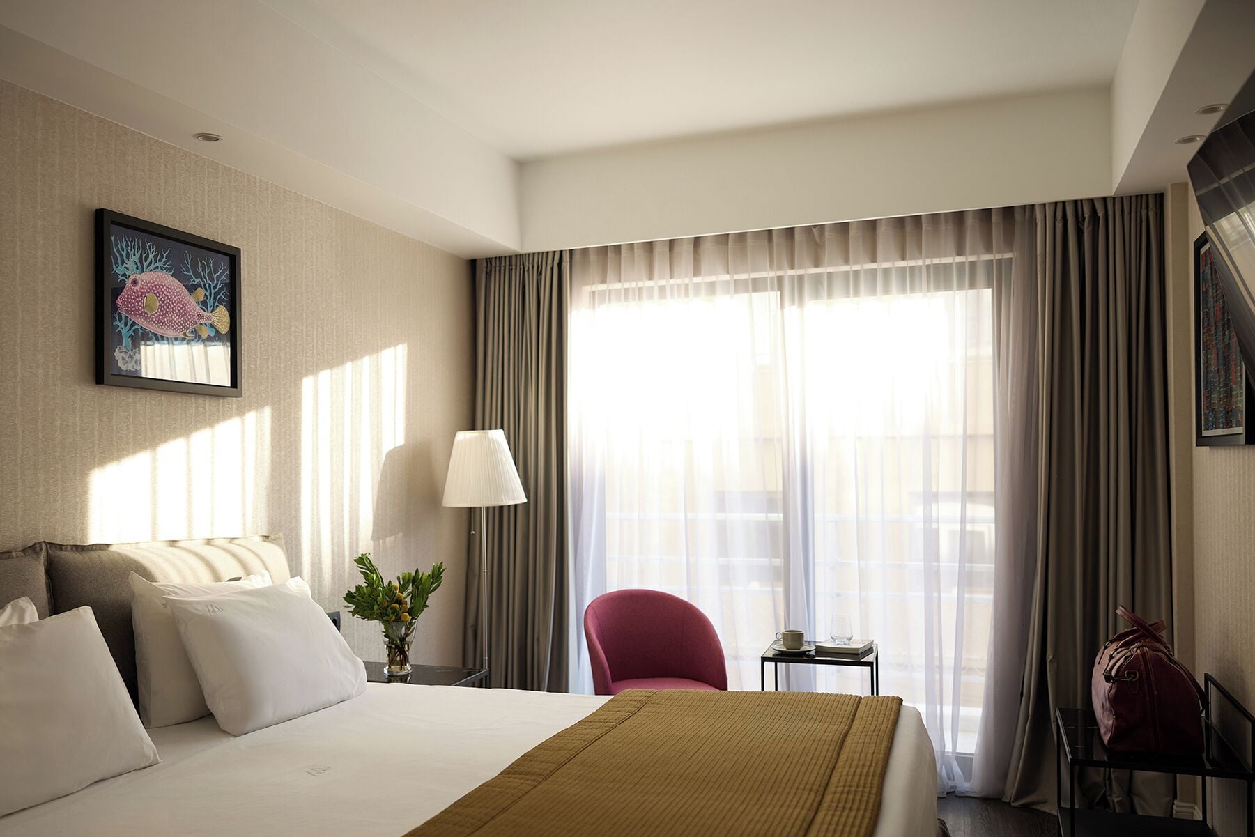 A hotel room with a bed, a desk, a chair, a lamp, and a window with curtains.