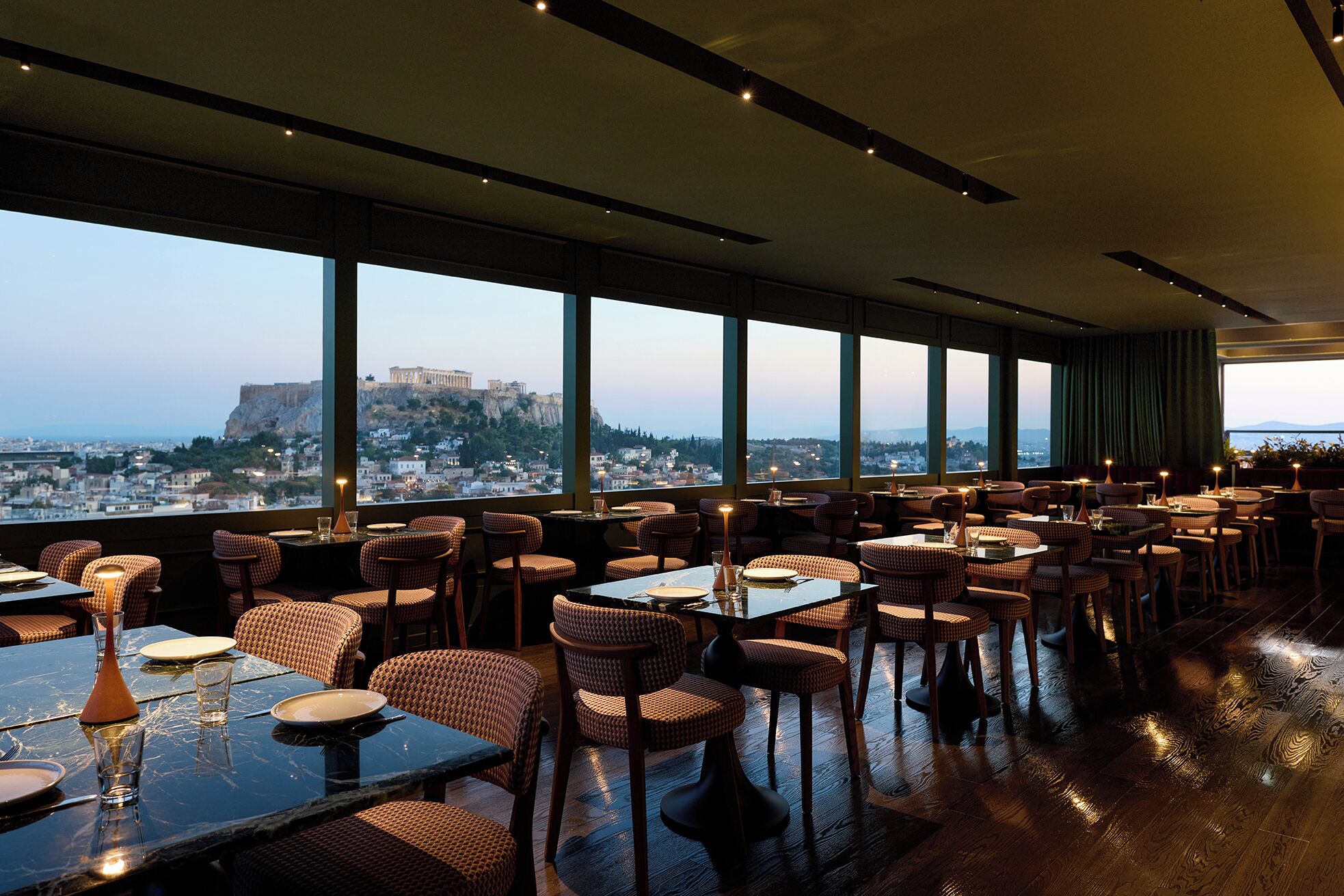 A restaurant with multiple tables and chairs, large windows with a view of a cityscape and a historic building.