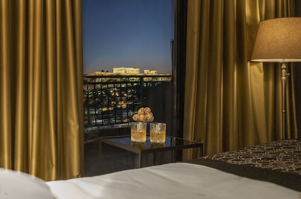 A hotel room with a view of ancient Greek architecture, a bedside table with two glasses, and a lamp. - Astor Hotel Athens (Athens)
