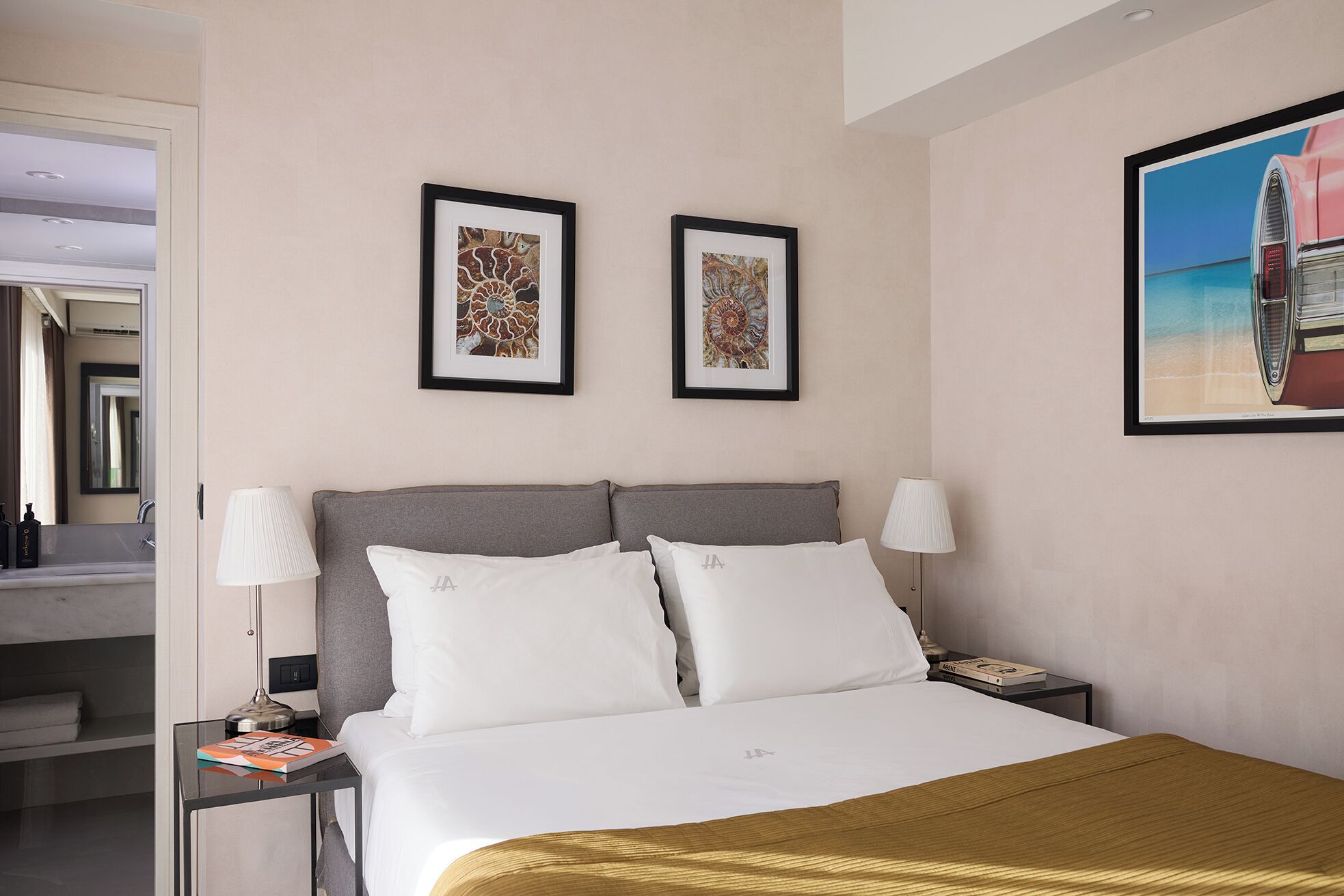 A hotel room with a bed, two framed pictures, a nightstand, and a night lamp.