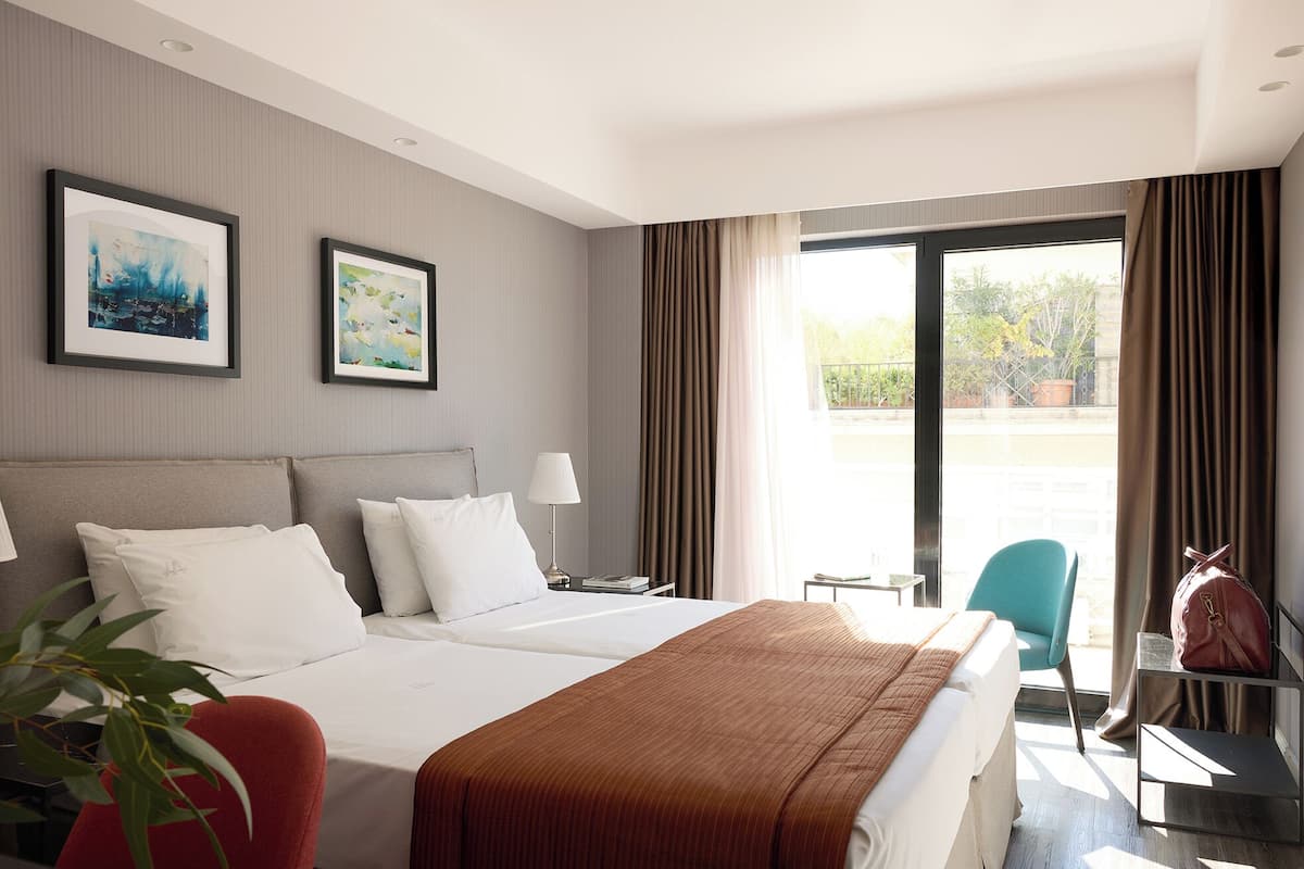 A hotel room with a bed, two bedside tables, a chair, a lamp, and a view of the outdoors.