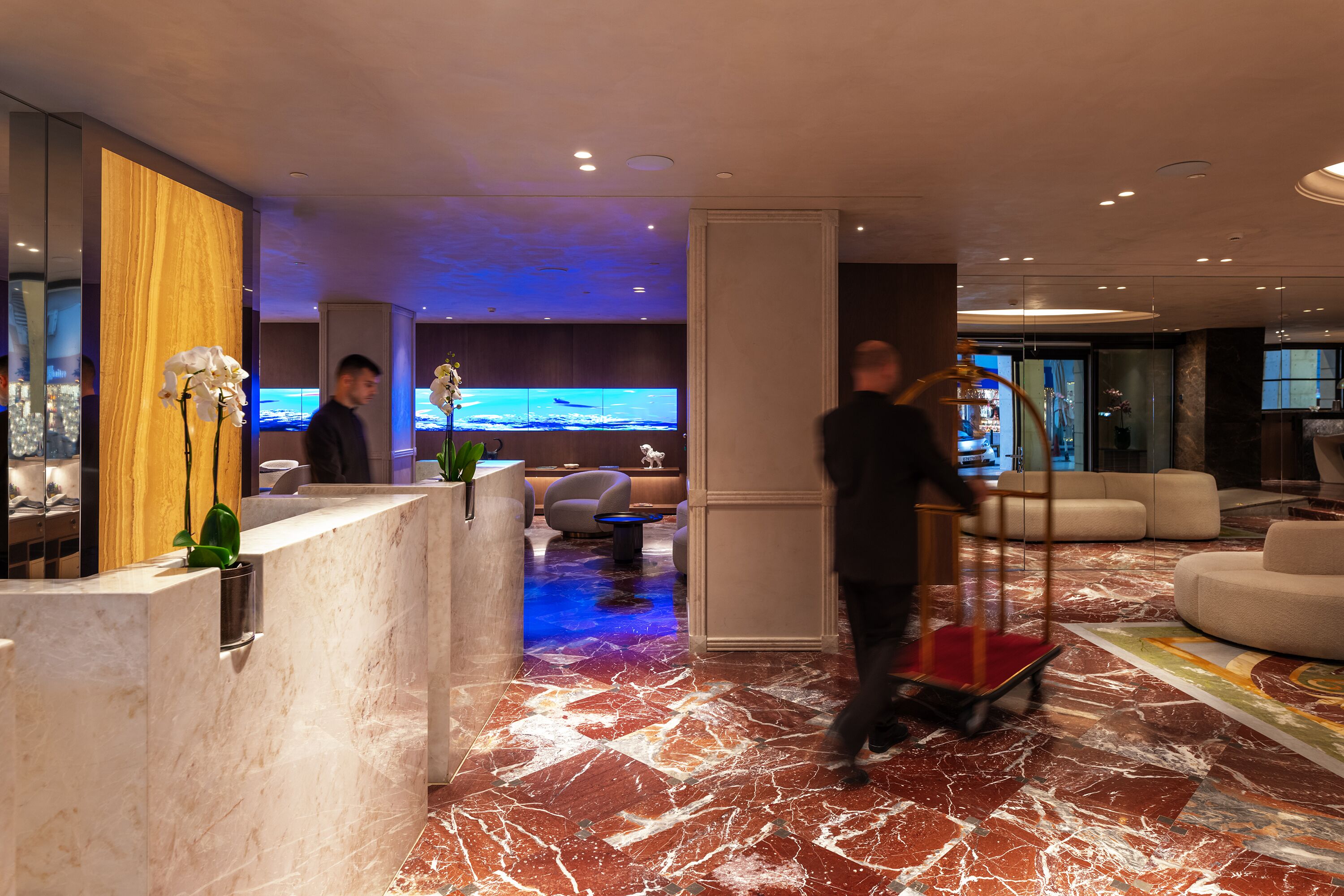 Un hall d’hôtel doté d’un sol en marbre, d’un comptoir d’accueil, d’un espace salon et d’un grand téléviseur à écran plat.
