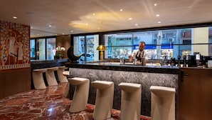 Un área de bar moderna con suelo de mármol, una barra con un barista y vista a la calle.