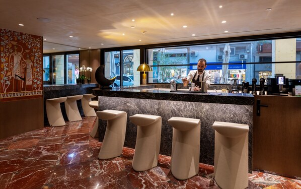 Un espace bar moderne avec un sol en marbre, un comptoir où travaille un barista et une vue sur la rue.