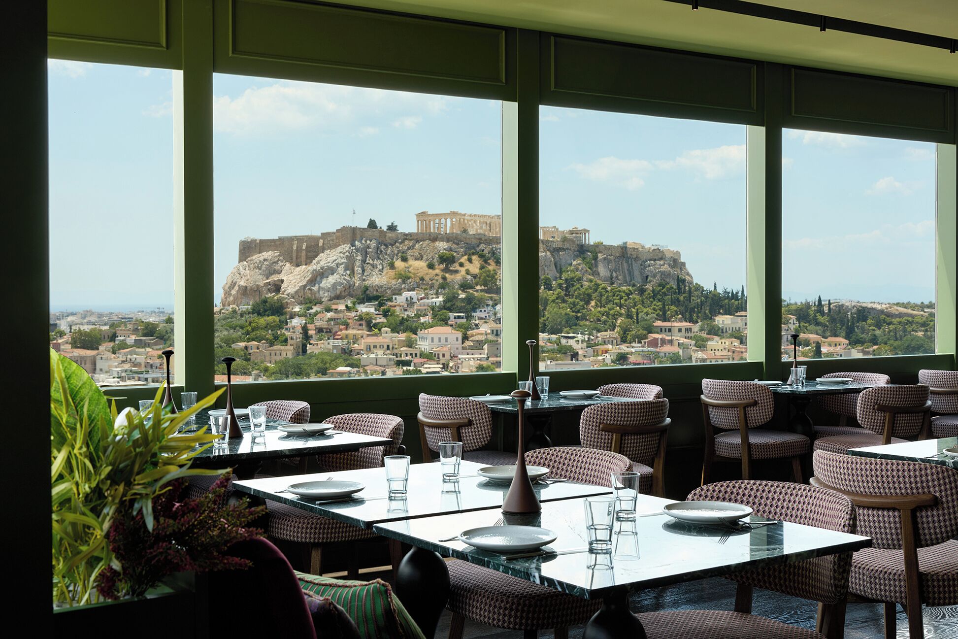 A restaurant with tables and chairs, large windows with a view of a historic fort on a hill.