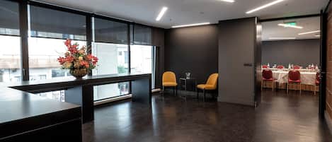 Un moderno vestíbulo de hotel con mostrador de recepción, amplias ventanas y un comedor con sillas rojas y una mesa.
