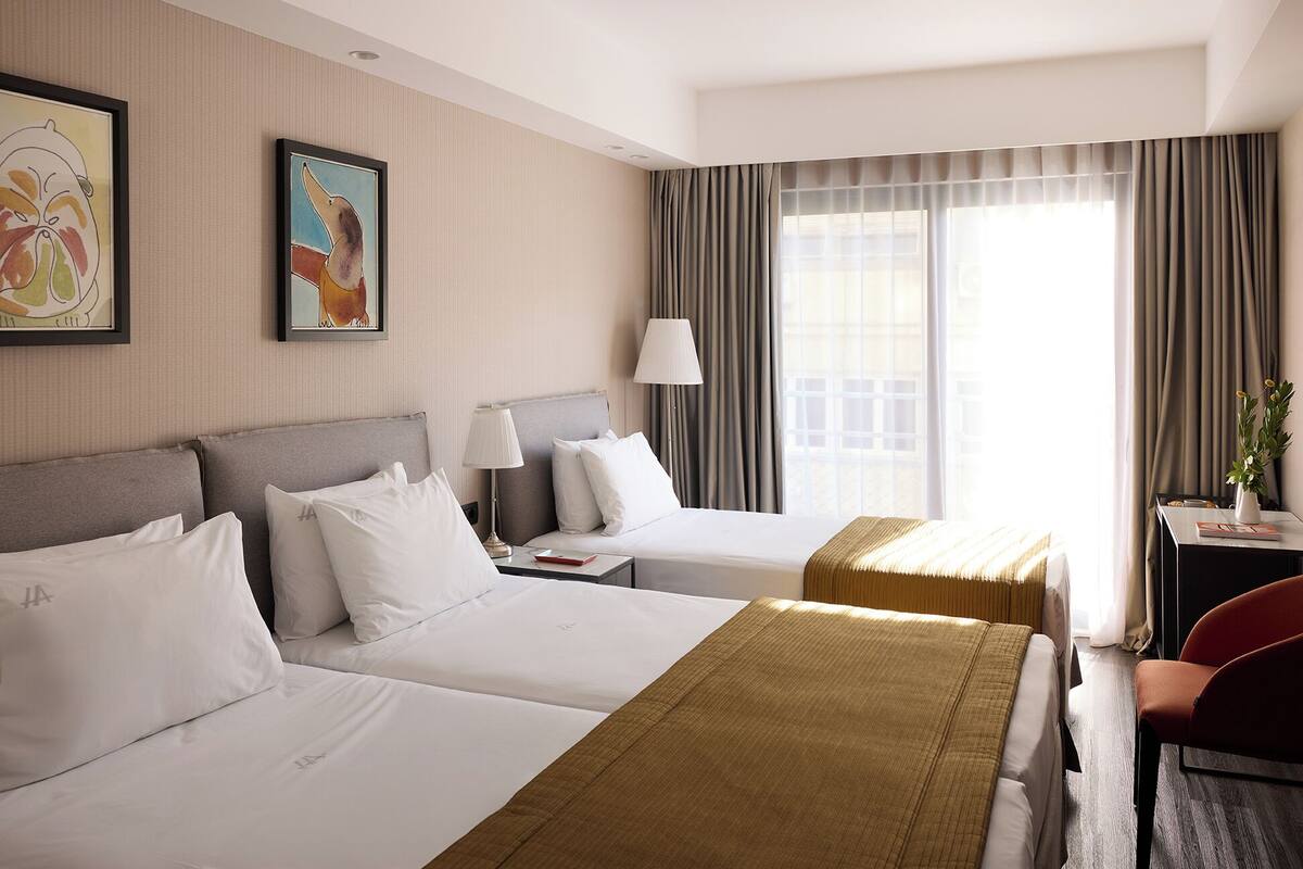 A hotel room with two beds, a desk, a chair, and a window with curtains.