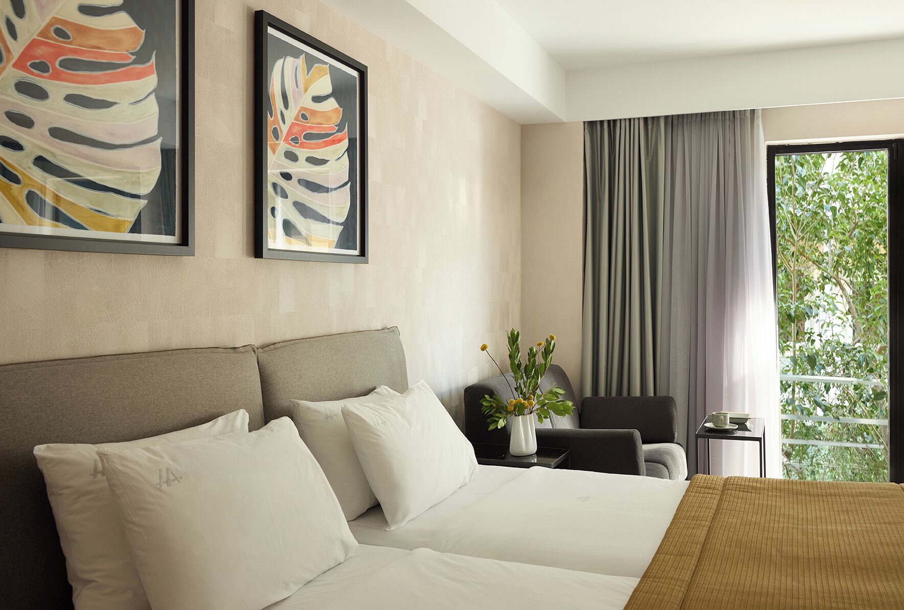 Habitación de hotel con una cama grande, una silla, una mesita con un jarrón de flores y una ventana con cortinas.