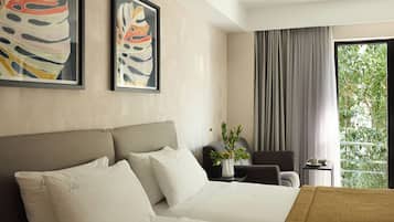 A hotel room with a large bed, a chair, a small table with a vase of flowers, and a window with curtains.