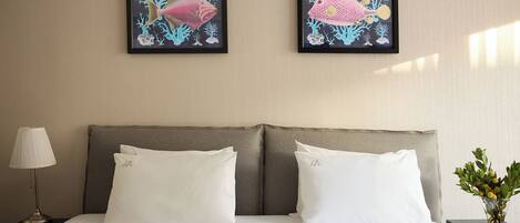 A hotel room with a bed, two white pillows, a nightstand with a lamp, and two framed pictures of fish on the wall.