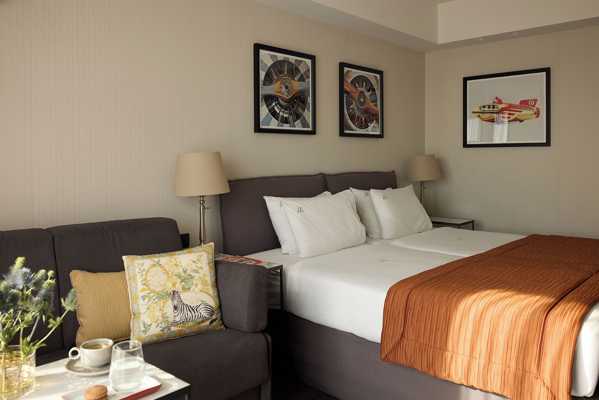 A hotel room with a bed, a sofa, two lamps, a table with a tray, and three framed pictures on the wall.