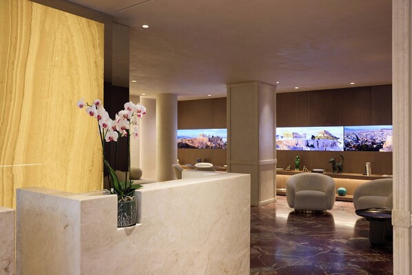A modern lobby with marble reception desk, comfortable seating, and large screens displaying cityscapes. - Astor Hotel Athens (Athens)