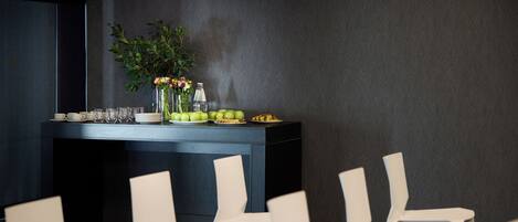 Un salón de conferencias con una pared gris oscuro, una mesa negra con una planta y varias sillas blancas.