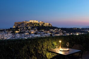 Uma mesa com uma vela e um copo de vinho, com vista para uma cidade e uma antiga fortaleza imponente numa colina.